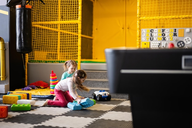 Two sisters playing at kids play center while build with colored plastic blocks