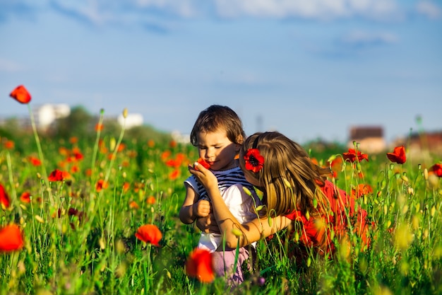 Two sisters in poppy field sniffing flowers in summer day