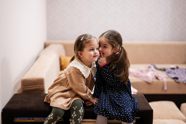 Two sisters sit on the sofa and tell and share girlish secrets with each other