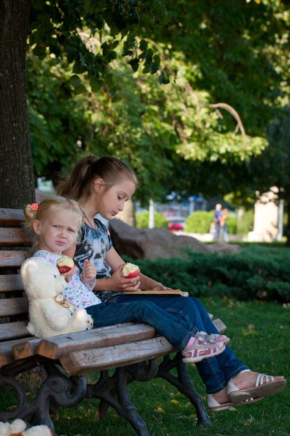 Two sisters sitting  on a bench at the park.