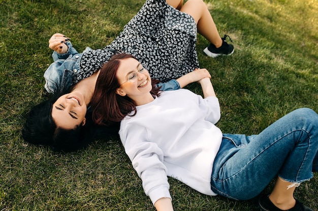 Two sisters smiling spending time outdoors lying on green grass in a park