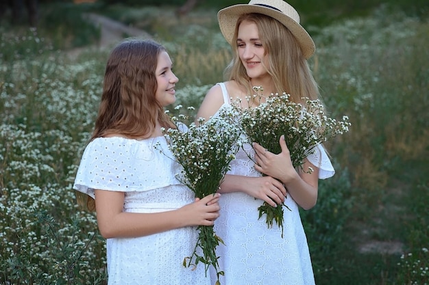 2 人の姉妹が牧草地に立ち、白いドレスを着て微笑む