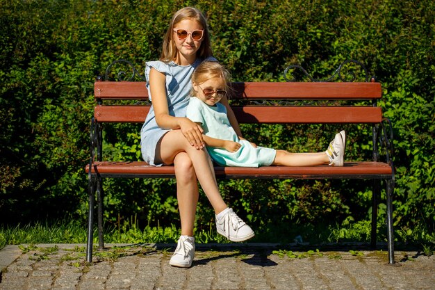 Two sisters in sunglasses sit in the park on a bench in summer