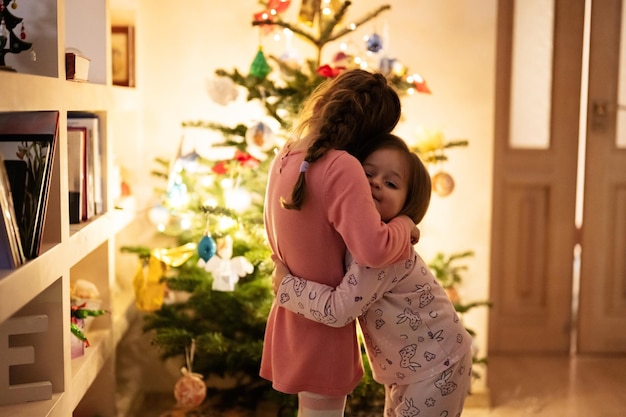 Two sisters together near Christmas tree at evening home