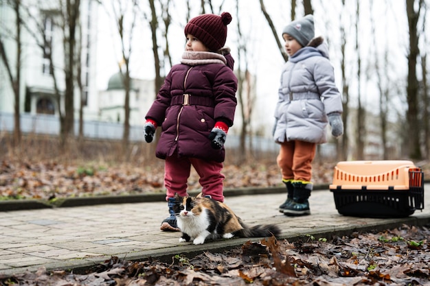 Two sisters with cat and travel plastic cage carriage outdoor at park