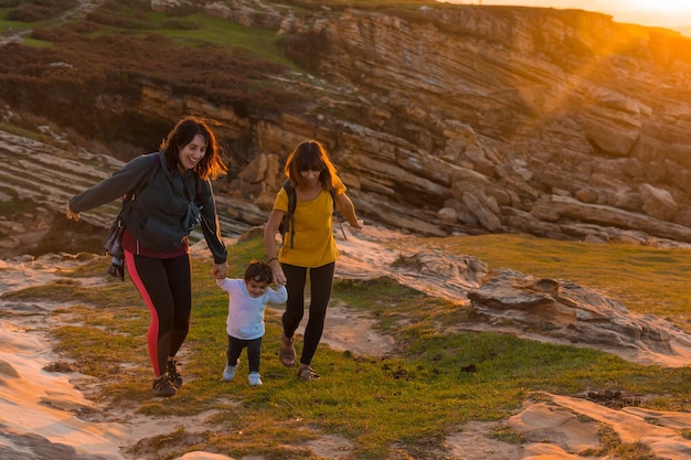 Two sisters with a child watching the sunset on the coast by\
the sea family lifestyle