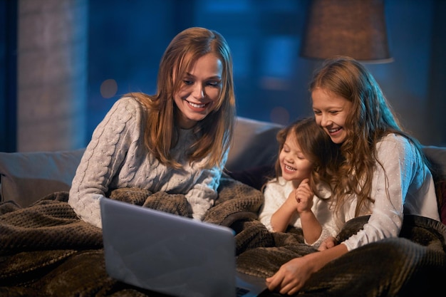 Two sisters with mother sitting on couch and using laptop