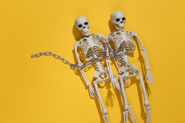Photo two skeletons wrapped in chain on a yellow bright background