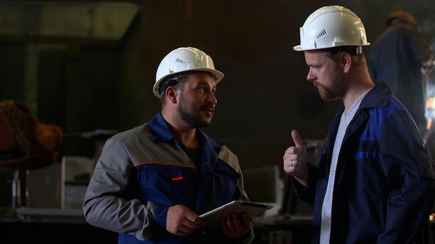 Two skillful factory engineer or worker discussing project on tablet computer