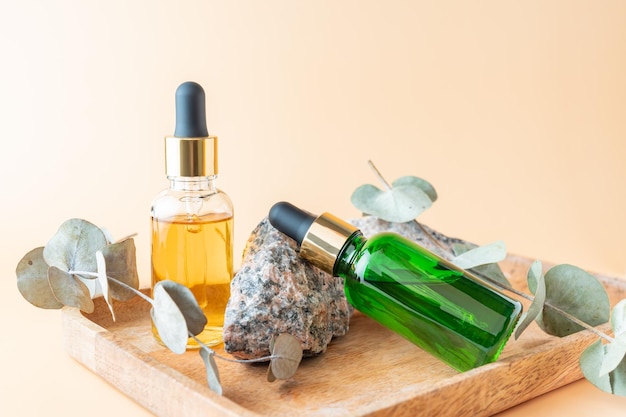 Two skin serum bottles next to natural stone and dry eucalyptus against beige background with copy space Concept of luxury skin serum for anti aging treatment