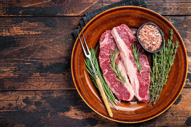 Two sliced Raw Striploin steaks or New York steaks, beef meat. Dark wooden background. Top view. Copy space.