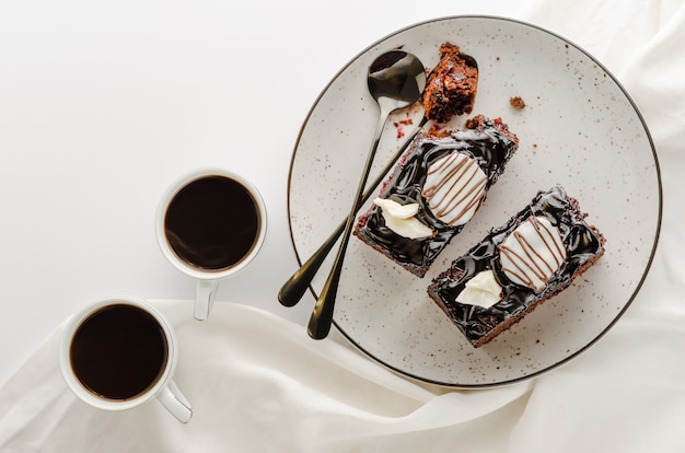 艶をかけられたチョコレートケーキと白い背景の上のコーヒーの2つのスライス