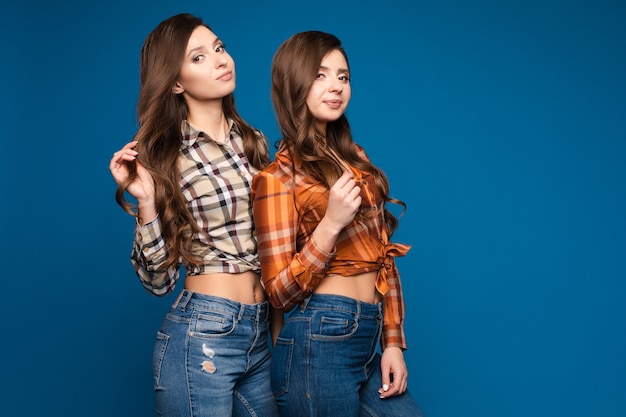 Two slim sisters in checkered shirts and jeans posing