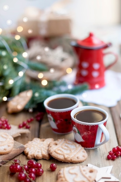 2つの小さなコーヒーカップとコーヒーポット、ベリーとクッキーのケーキ、ギフト、窓の近くの村のテーブルのクリスマスツリーの近く