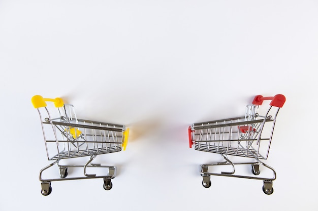 Two small empty decorative shopping carts with yellow, red accents on white background, place for text. View from above. Mockup, copy space. Concept business, finance, retail, online shopping.