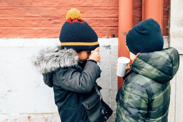 Two small friends of different ethnicity eat a milkshake while dribbling their jackets