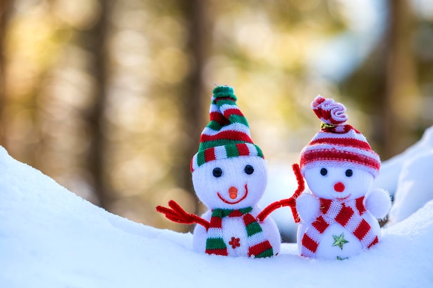 Two small funny toys baby snowman in knitted hats and scarves in deep snow outdoors on bright blue and white copy space background Happy New Year and Merry Christmas greeting card