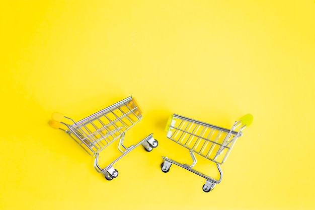 Two small miniature metal supermarket trolleys for shopping isolated on bright mint colour yellow background. Top view. Copy space for text. Shopping, purchases, sale concept.