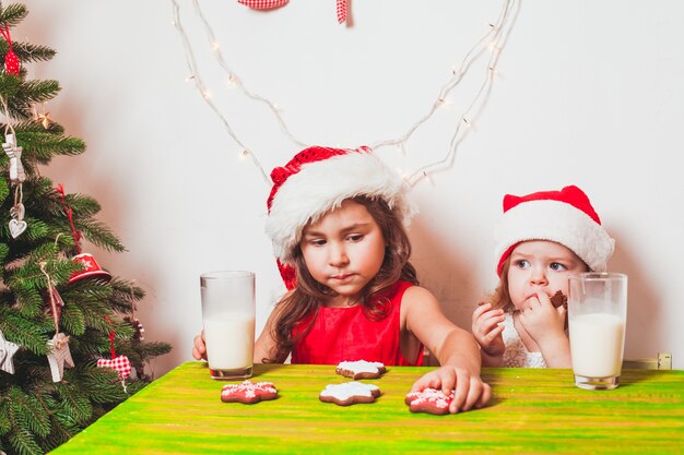 Two small Santas are drinking milk and eating colorful gingerbreads