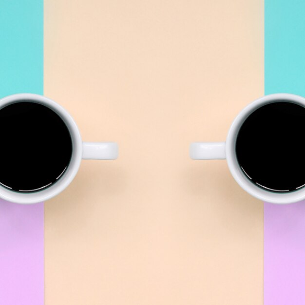 Two small white coffee cups on pink, blue, coral and lime colors paper