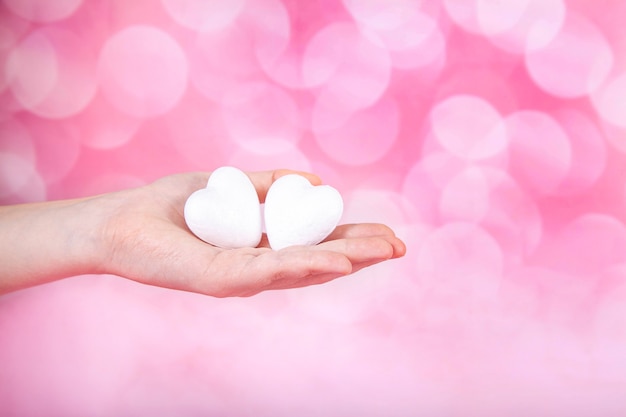 Foto due piccoli cuori bianchi in mano su sfondo rosa con bohe. biglietto di auguri di san valentino