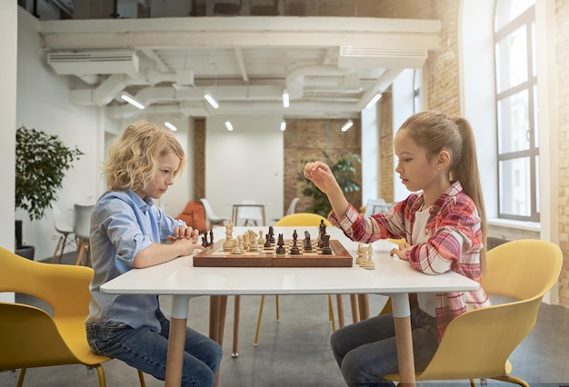 Two smart little children boy and girl developing chess strategy playing board game sitting