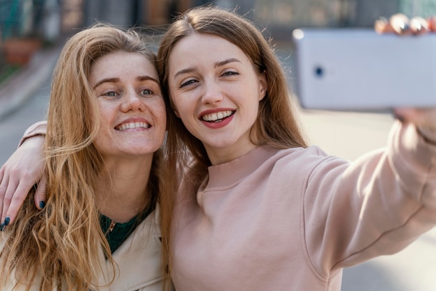 Foto due amiche di smiley all'aperto nella città che prendono un selfie