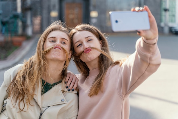 Foto due amiche di smiley all'aperto nella città che prendono un selfie