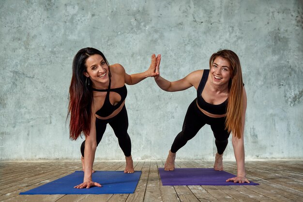Две улыбающиеся красивые, фитнес девушки делают упражнения в тренажерном зале дают по пять. Концепция спорта, работа в команде.
