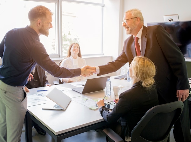 Two smiling businessman shaking hands together in the board meeting