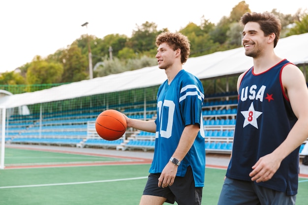 Two smiling confident basketball players walking at the playground, ready to play basketball