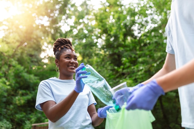 Two smiling diverse young male volunteers putting trash in garbage bags during a community cleanup day in a field