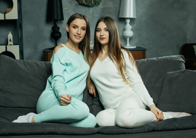 Two smiling friends women sitting on the couch looking at camera in sitting room at home