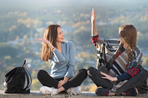 Две улыбающиеся девушки с удовольствием сидят на холме