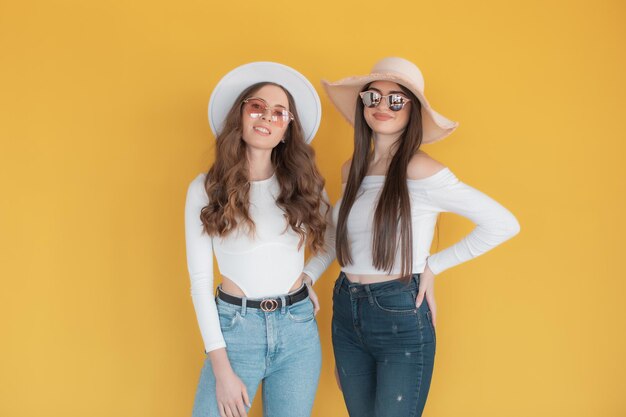 Two smiling girls in sunglasses posing together and looking at the camera on yellow