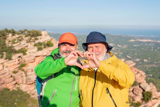 Foto due amici escursionisti sorridenti che fanno una forma a cuore con le mani stile di vita sano amore per se stessi e concetto di pensionamento attivo