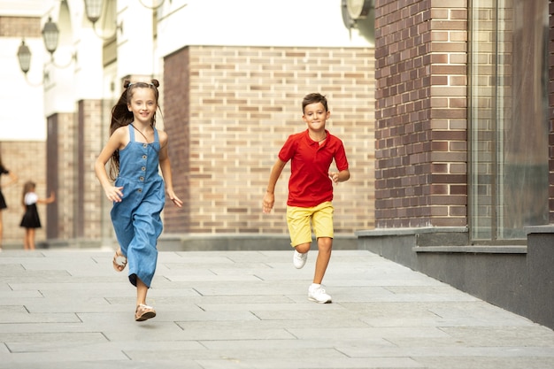 Two smiling kids boy and girl running together in town city in summer day