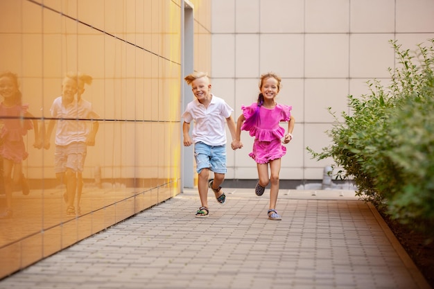 Two smiling kids, boy and girl running together in town, city in summer day