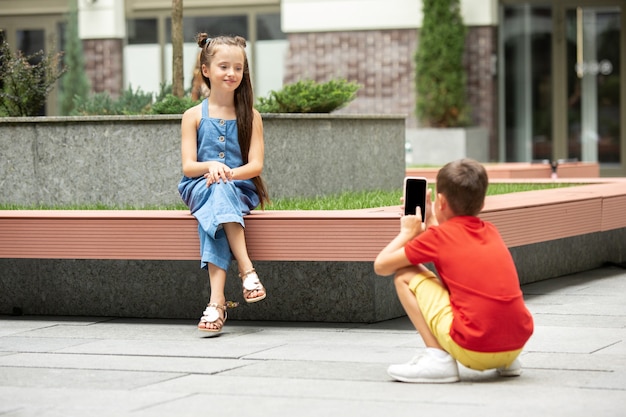 夏の日に町、街で一緒に写真を撮る2人の笑顔の子供、男の子と女の子