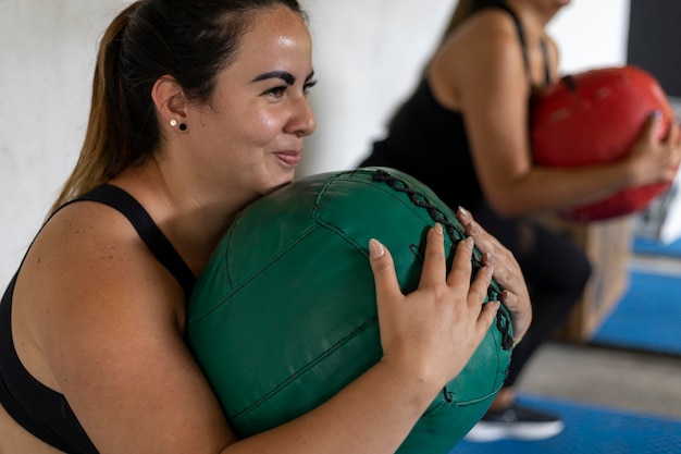 Two smiling Latin American women holding a medicine ball during functional training at the gym Healthy lifestyle concept