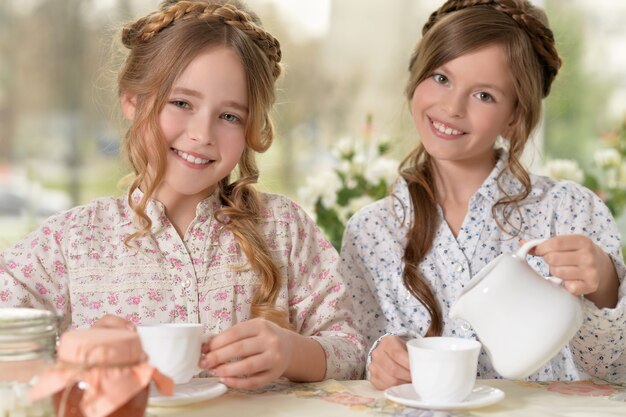 Two smiling little girls drinking tea at home