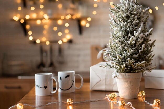 Two smiling mugs at modern kitchen designed in white color and decorated for Christmas