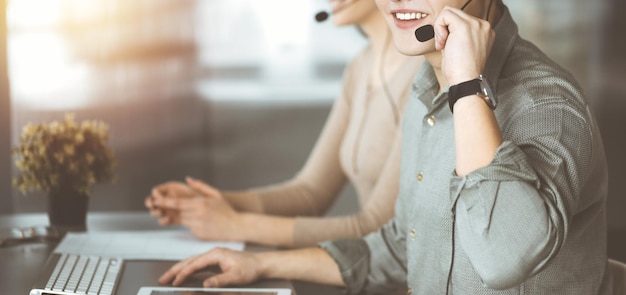 Foto due persone sorridenti con le cuffie stanno parlando con i clienti mentre sono seduti alla scrivania in un ufficio moderno e soleggiato