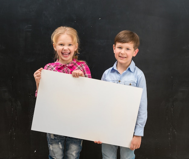 Two smiling schoolchildren with blank sheet of paper