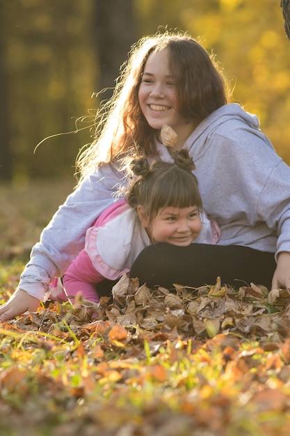 Two smiling sisters sitting on the ground in yellow autumn park