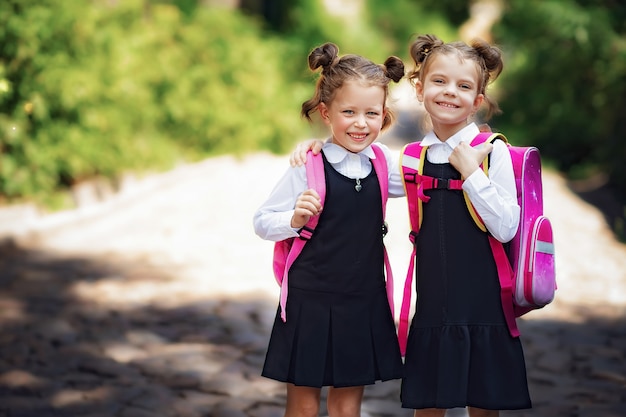 学校のバックパックを着て2つの笑顔の学生の女の子。小学校の外の幸せな白人少女の肖像画。カメラを見て笑顔の女子高生