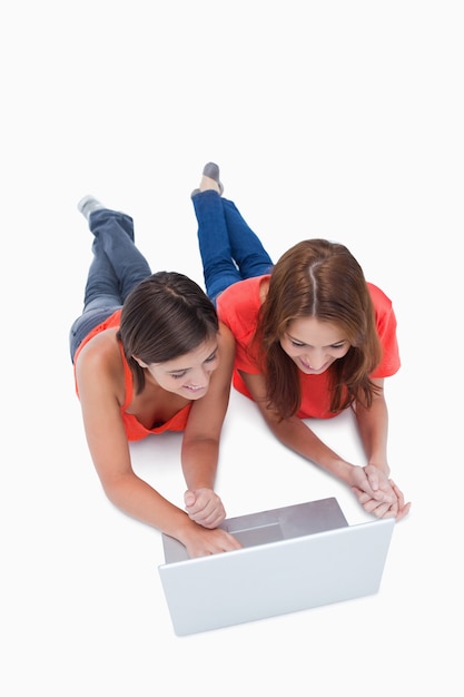 Two smiling teenage girls lying down while looking at a laptop