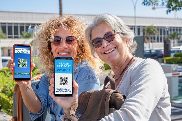 Due donne sorridenti pronte a viaggiare mostrando la certificazione sanitaria digitale per le persone vaccinate contro il coronavirus. madre e figlia felici e spensierate