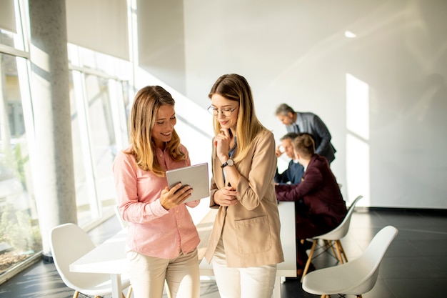 Two smiling young women looking on digital tablet at the office