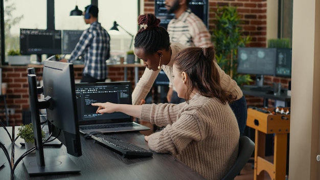 Two software coders analyzing source code looking for errors running on laptop screen while sitting at desk. Team of system engineers working on cyber security innovation in busy server room.